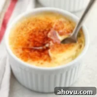 A close-up picture of a white ramekin filled with crème brûlée and a spoon inside of it.
