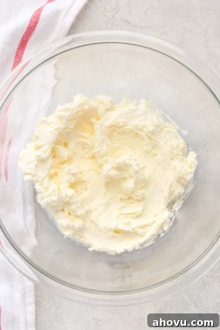 Velvet Chocolate Cream Cheese Bliss 3 A clear glass mixing bowl holding butter and cream cheese combined together with a red and white napkin in the background.
