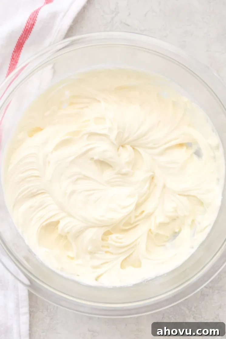 Velvet Chocolate Cream Cheese Bliss 4 A clear glass mixing bowl holding cream cheese frosting ingredients with a white and red napkin in the background.