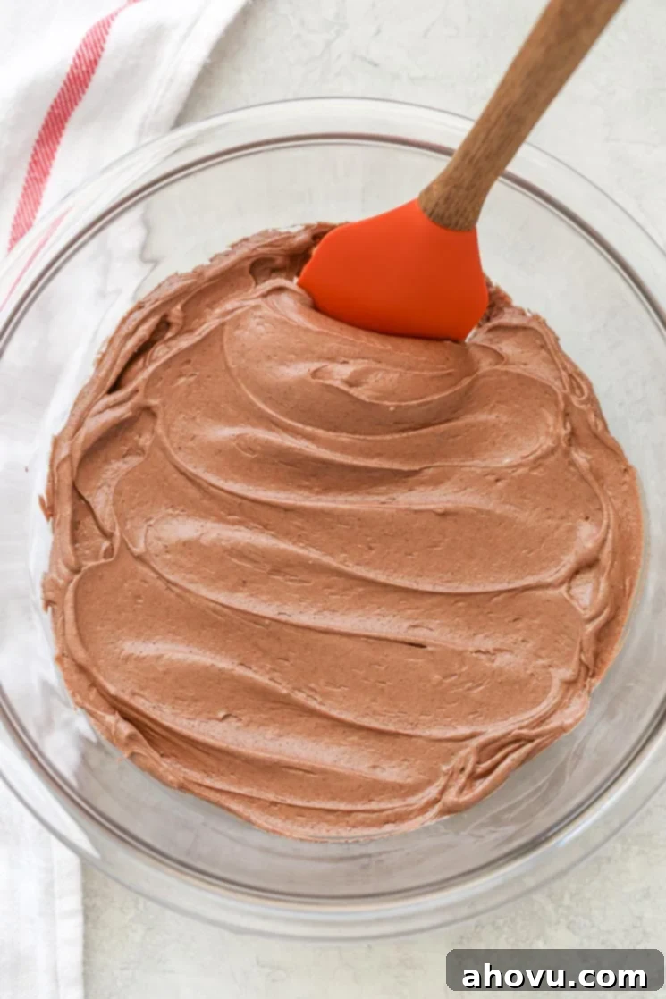 Velvet Chocolate Cream Cheese Bliss 5 A clear glass mixing bowl filled with chocolate cream cheese frosting and a rubber spatula.
