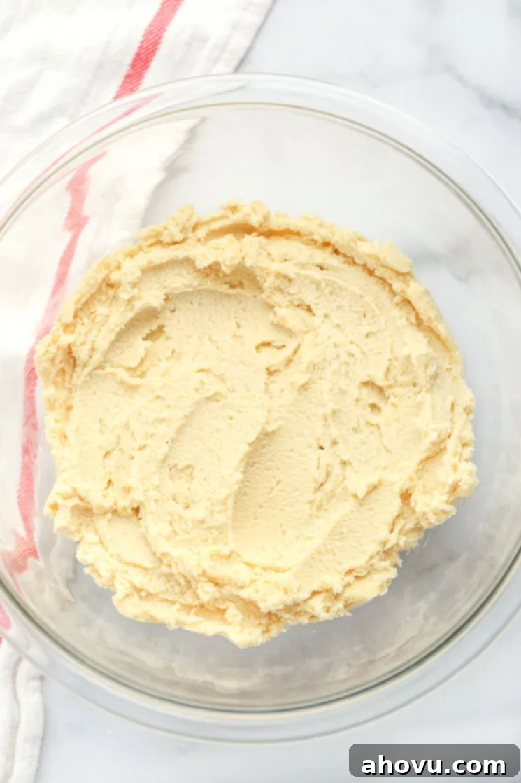 A clear glass mixing bowl filled with shortbread cookie dough and a red and white napkin in the background. 
