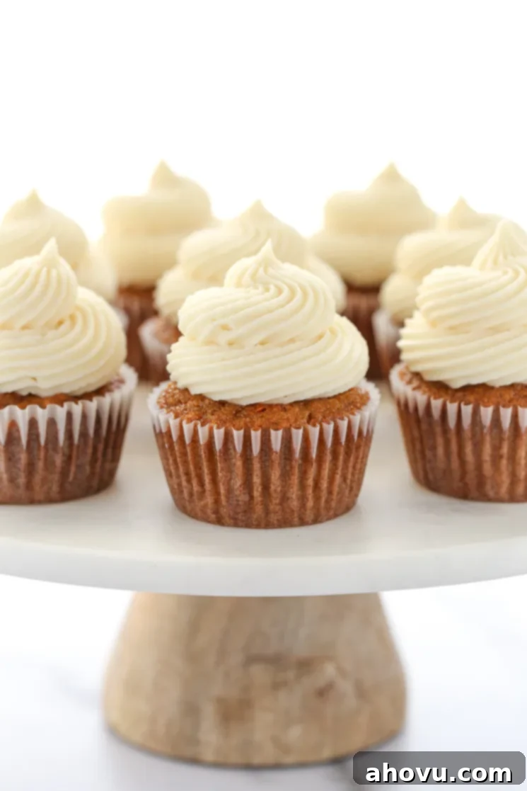 Perfectly Spiced Carrot Delights 2 A group of carrot cake cupcakes topped with cream cheese frosting resting on top of a marble cake stand with wooden base.