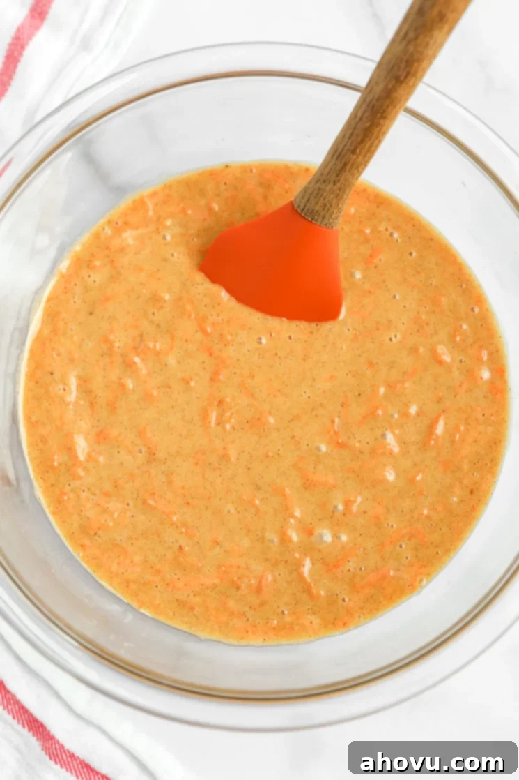 Perfectly Spiced Carrot Delights 3 A glass bowl filled with carrot cake cupcake batter and a rubber spatula on the side.