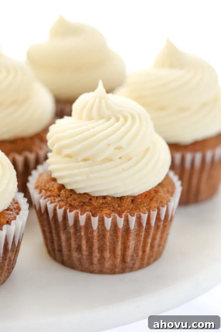 Perfectly Spiced Carrot Delights 6 A close up picture of carrot cake cupcakes topped with cream cheese frosting sitting on top of a marble cake stand.