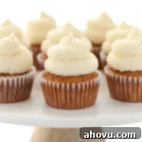 Perfectly Spiced Carrot Delights 7 A group of carrot cake cupcakes topped with cream cheese frosting setting on top of a marble cake stand.