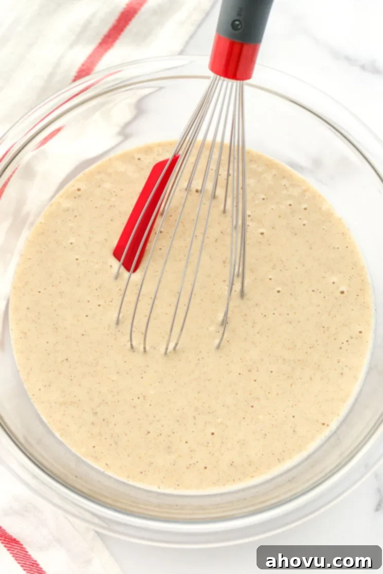 A clear glass bowl filled with funnel cake batter and a whisk. 