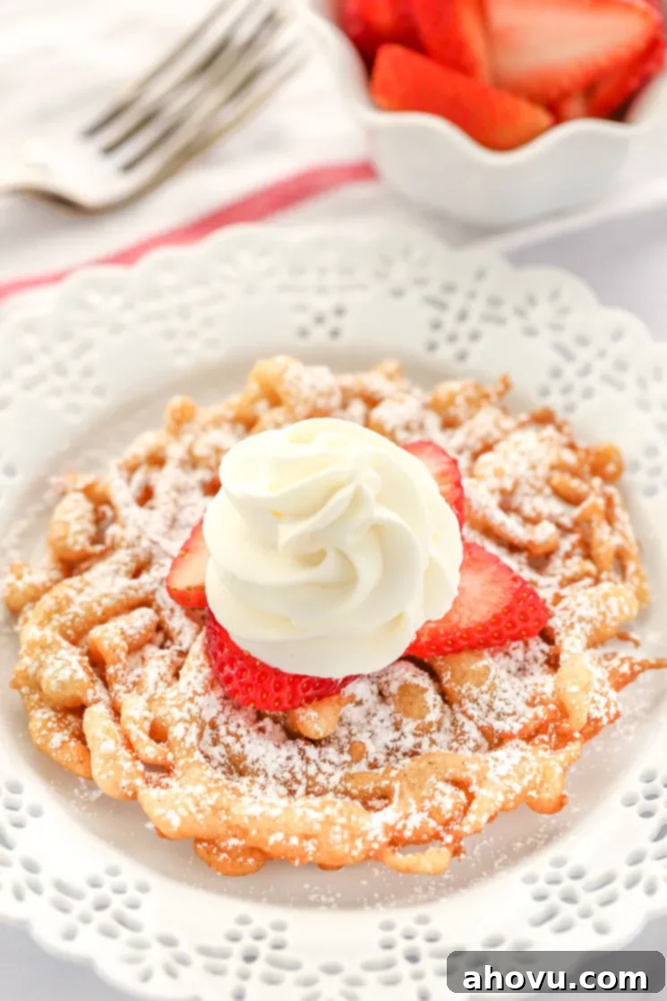A homemade funnel cake topped with strawberries and homemade whipped cream sitting on a decorative white plate.