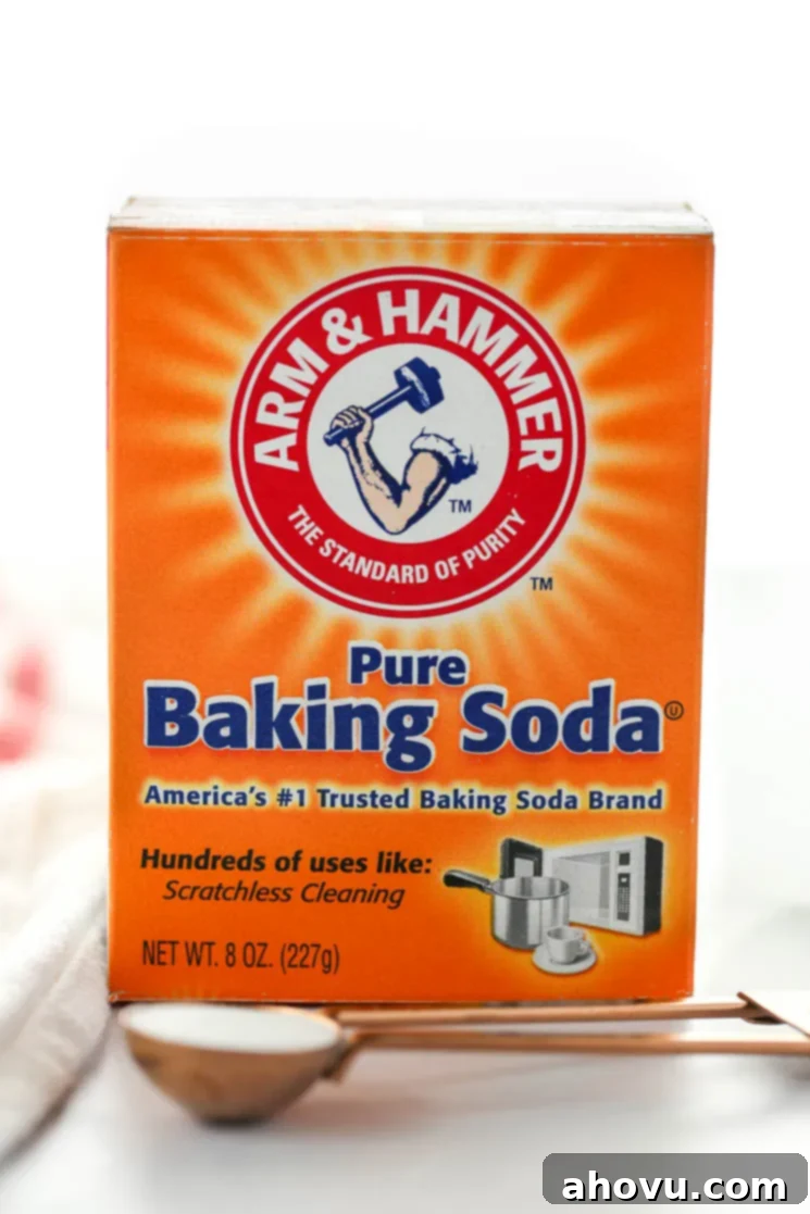 A box of baking soda behind a measuring spoon on top of a marble surface. 