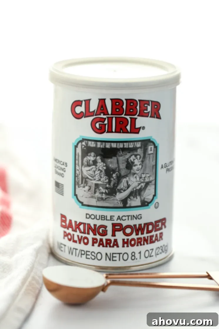 A can of baking powder behind a measuring spoon sitting on top of a marble surface. 