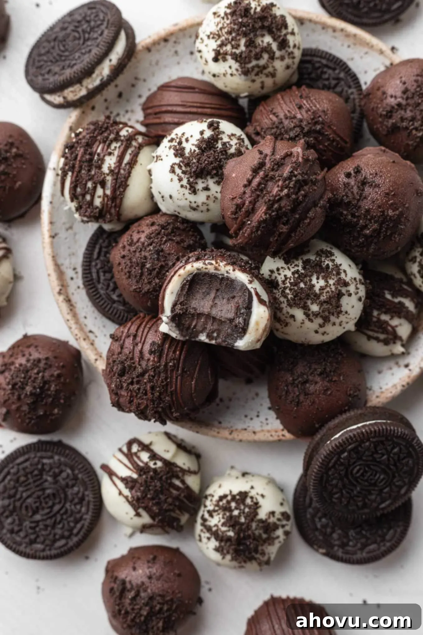 Velvet Oreo Truffles 5 An overhead view of a stack of Oreo cream cheese balls on a speckled white plate. One ball has a bite missing.