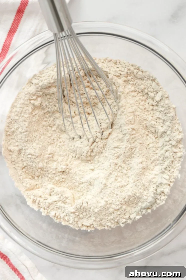 Sweet Nectar Cake 4 A clear glass mixing bowl filled with the precisely measured dry ingredients for a hummingbird cake, with a whisk resting on the side, ready for mixing.