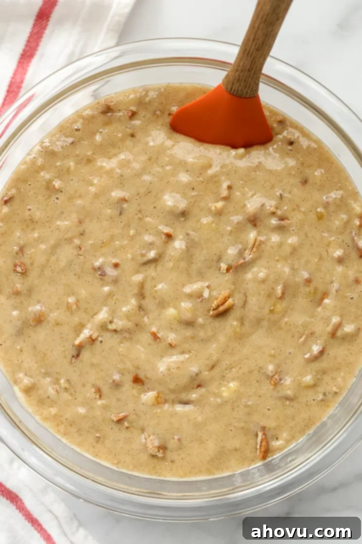 Sweet Nectar Cake 6 A wide glass bowl showcasing the perfectly mixed hummingbird cake batter, thick and rich, with a flexible rubber spatula resting on the rim, ready for baking.