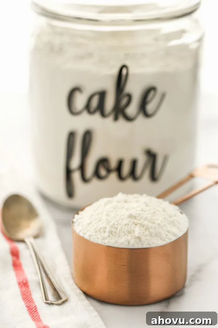 A copper measuring cup filled with cake flour and a container of flour in the background.