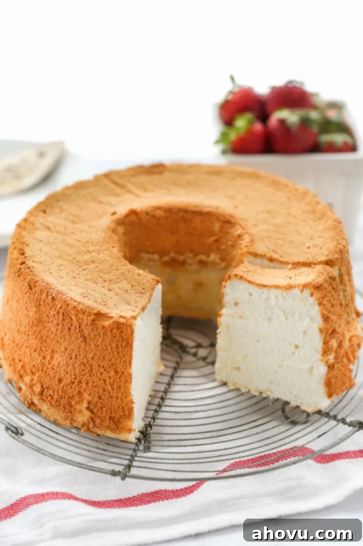 A pristine, light, and airy angel food cake sitting on a wire rack, garnished with fresh strawberries in the soft background.