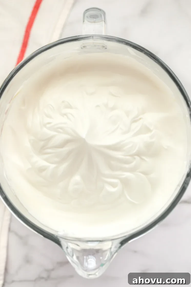 Room temperature egg whites beaten to stiff, glossy peaks in a clear glass bowl, ready for the next step of the angel food cake recipe.