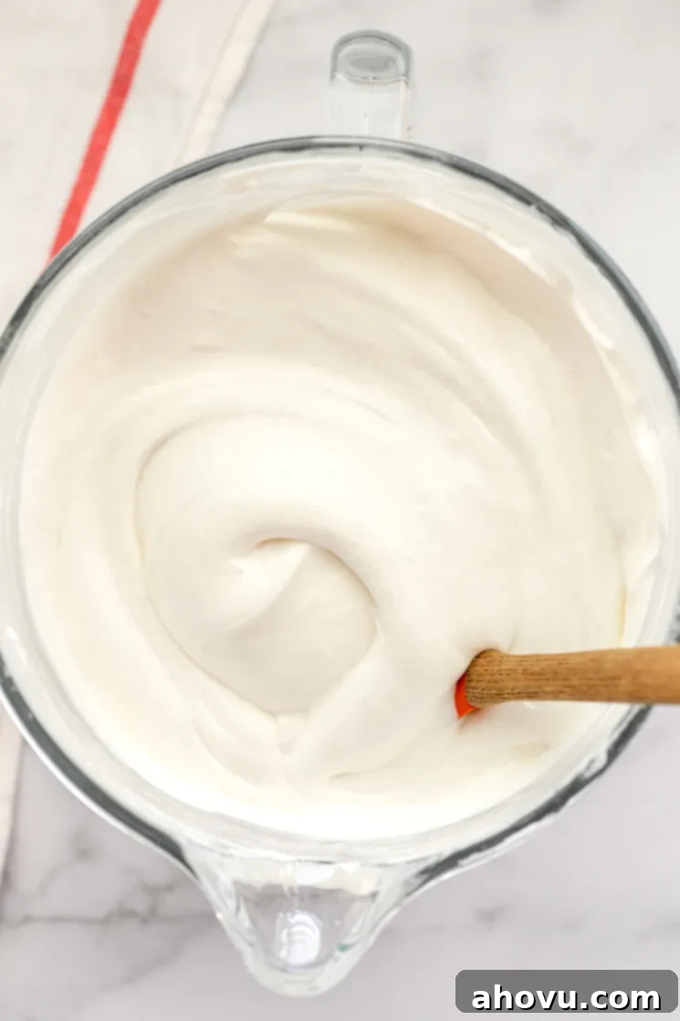 A glass bowl filled with the delicate, cloud-like angel food cake batter, with a rubber spatula resting on the side, ready for transfer to the pan.