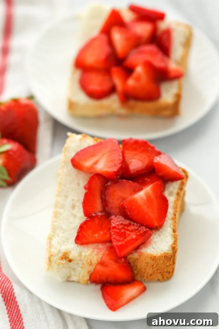 Beautifully sliced angel food cake pieces arranged on white plates, generously topped with fresh, vibrant sliced strawberries.