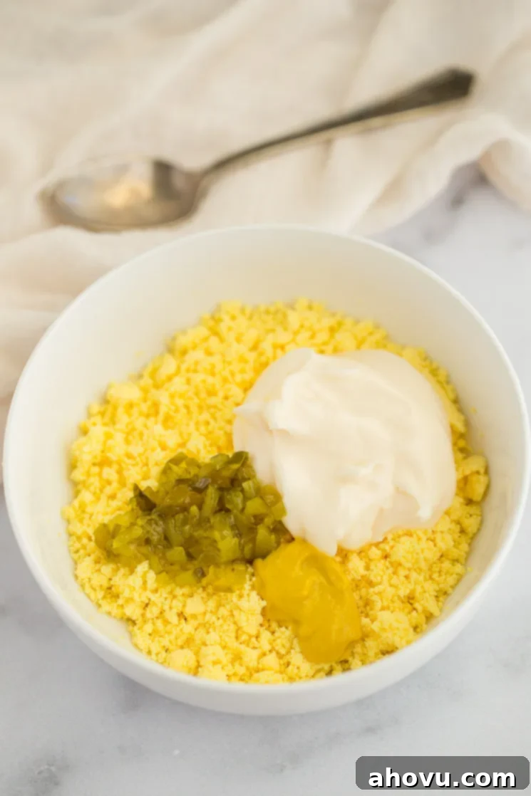 Spiced Yolk Delights 3 A white bowl filled with crumbled egg yolks, mayonnaise, mustard, and relish, ready to be mixed for deviled eggs.