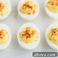 Spiced Yolk Delights 6 A close-up picture of deviled eggs on a piece of parchment paper, garnished with paprika.