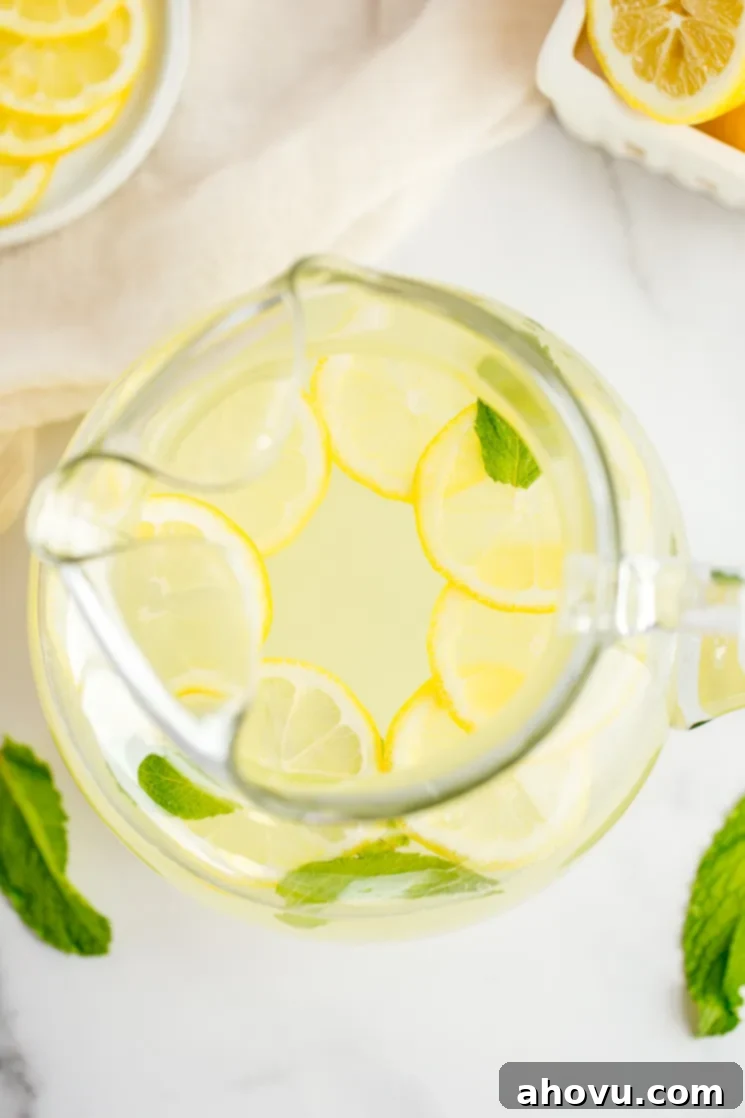 A large glass pitcher filled with homemade lemonade, lemon slices, and fresh mint leaves.