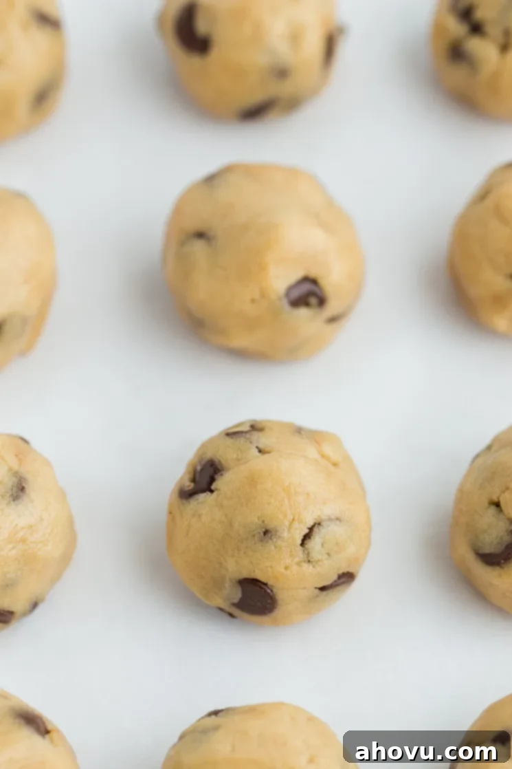 Perfectly portioned edible cookie dough rolled into smooth balls, neatly arranged on a piece of parchment paper, ready for storage or enjoyment.