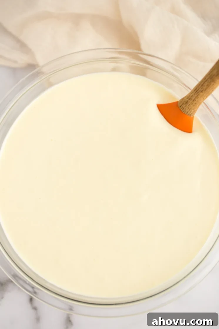 A pristine glass bowl filled with a creamy, pale yellow cheesecake filling, ready to be poured into the crust.