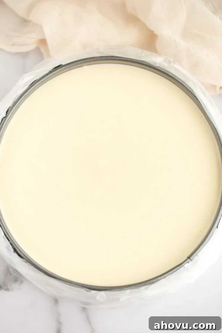 A springform pan, snugly wrapped in foil and placed inside an oven bag, filled with unbaked cheesecake filling, ready for its water bath.