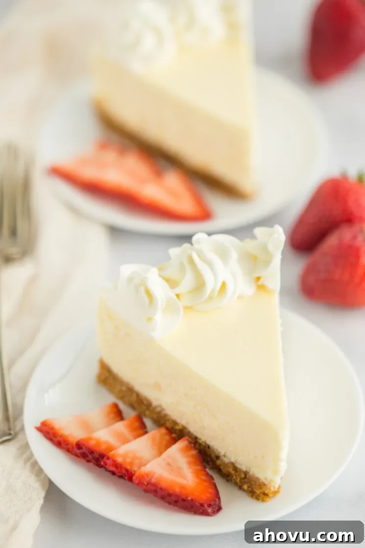 Two exquisite slices of classic cheesecake, each adorned with fresh, vibrant sliced strawberries, presented on elegant white plates.