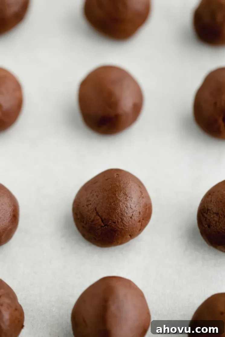 Cookie dough rolled into uniform balls and arranged on a piece of parchment paper, ready for baking.