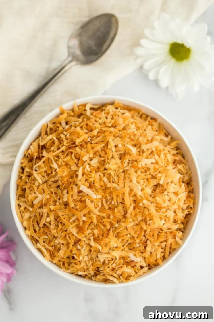A white bowl filled with perfectly toasted coconut, with an antique spoon and delicate flowers in the background, suggesting culinary elegance.