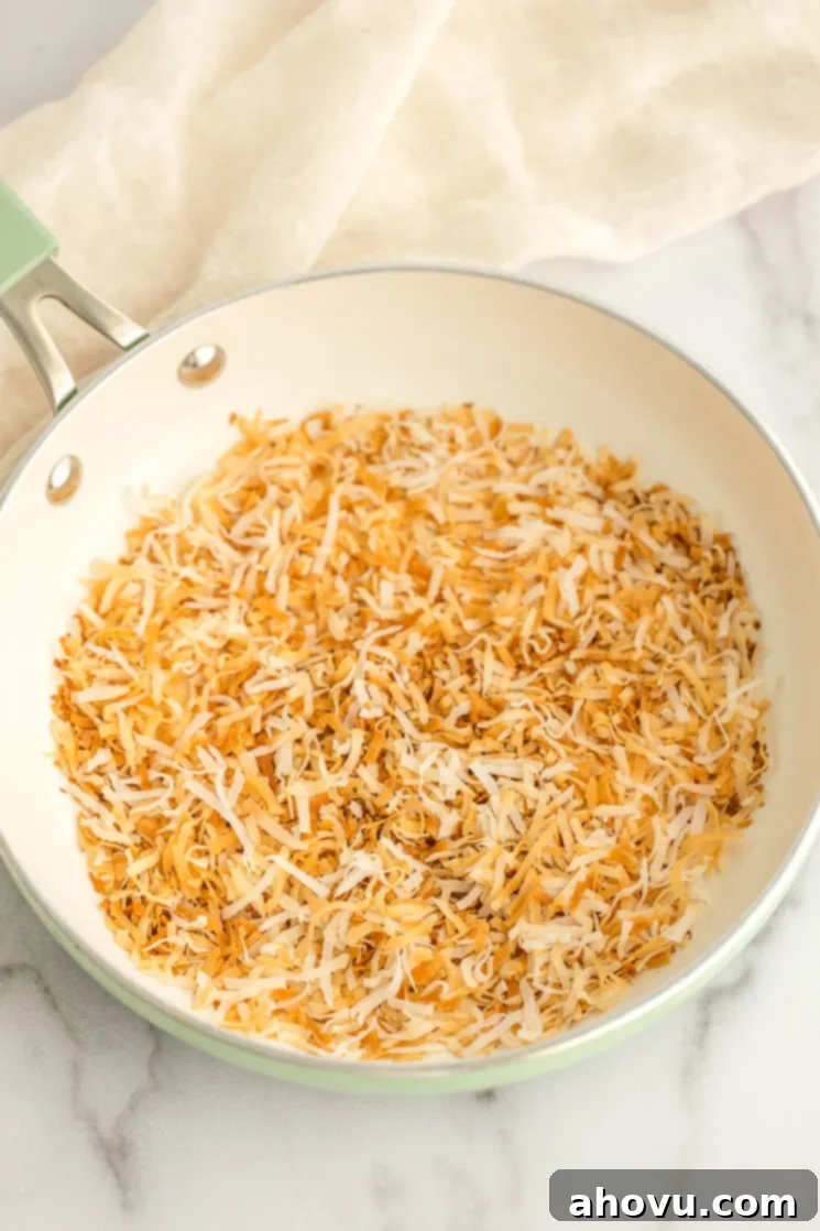 A batch of golden-brown toasted coconut residing in a vibrant green skillet on the stovetop.