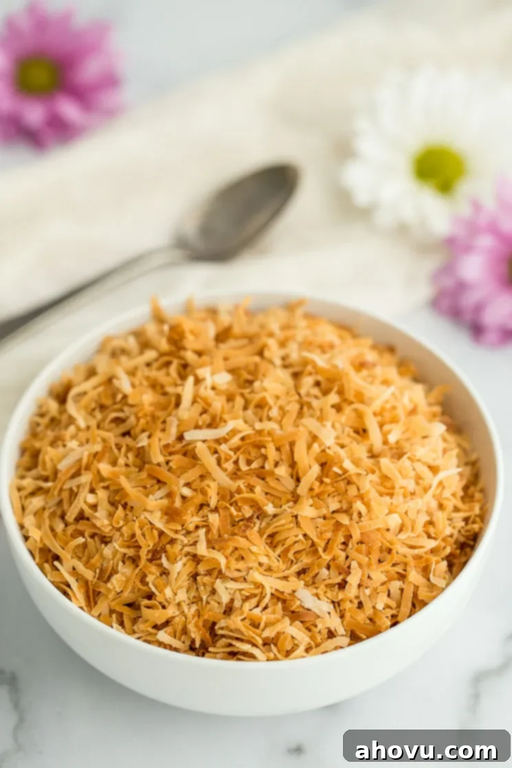 A white bowl filled with golden toasted coconut, perfectly showcased with an antique spoon and soft flowers in the background, ready for use.