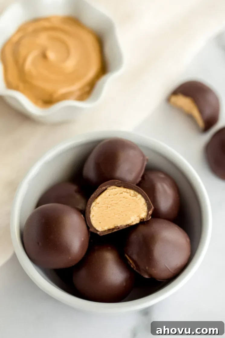 A white bowl filled with peanut butter balls and a small bowl of peanut butter in the background. 