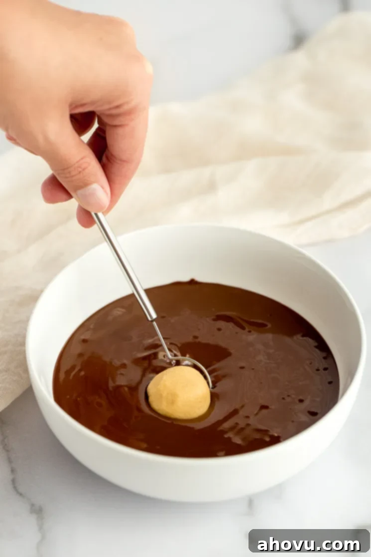 A white bowl filled with melted chocolate and a ball of the peanut butter mixture being dipped in it. 