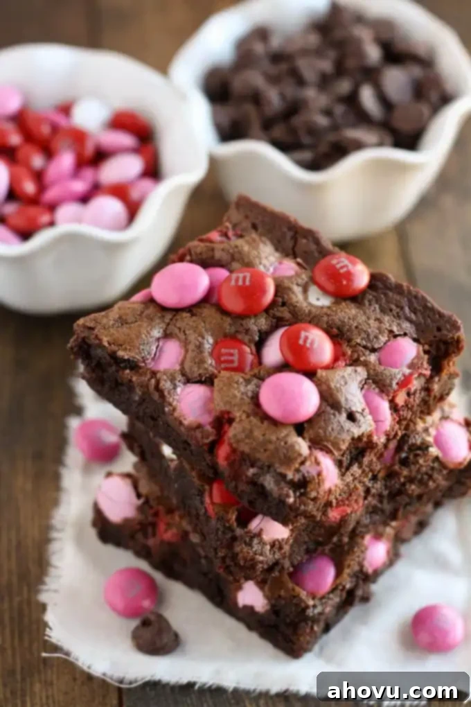 A stack of three Valentine brownies on a square of fabric. A bowl of M&M's and a bowl of chocolate chips are in the background.