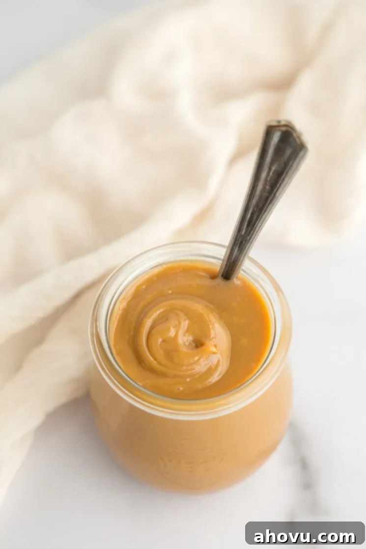 A glass jar filled with golden-brown dulce de leche, accompanied by an antique silver spoon for serving.