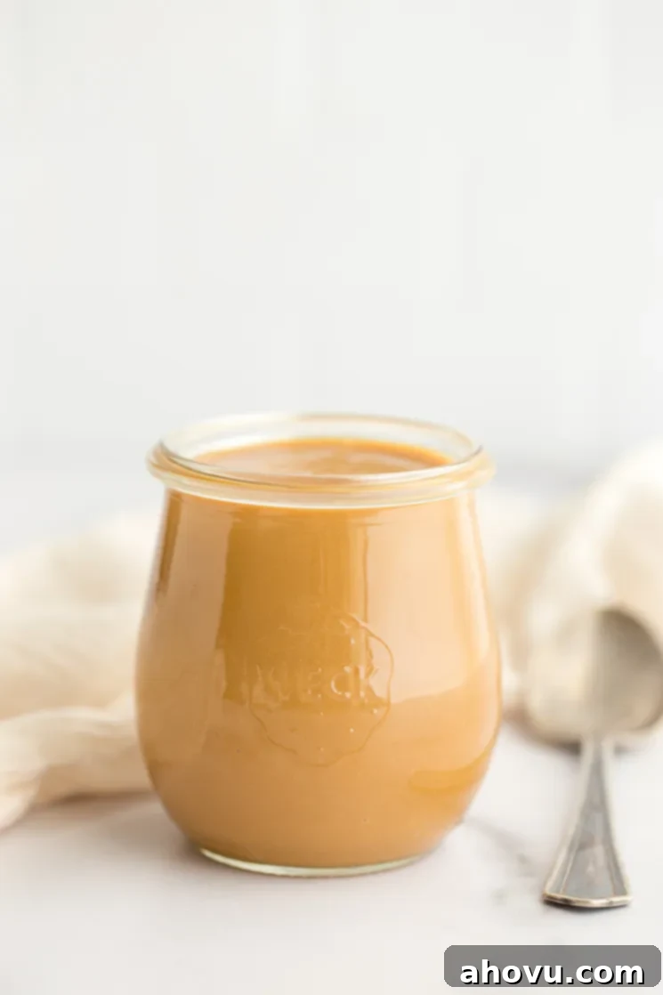 A charming glass jar of homemade dulce de leche, perfectly golden and smooth, resting on a sleek marble surface.