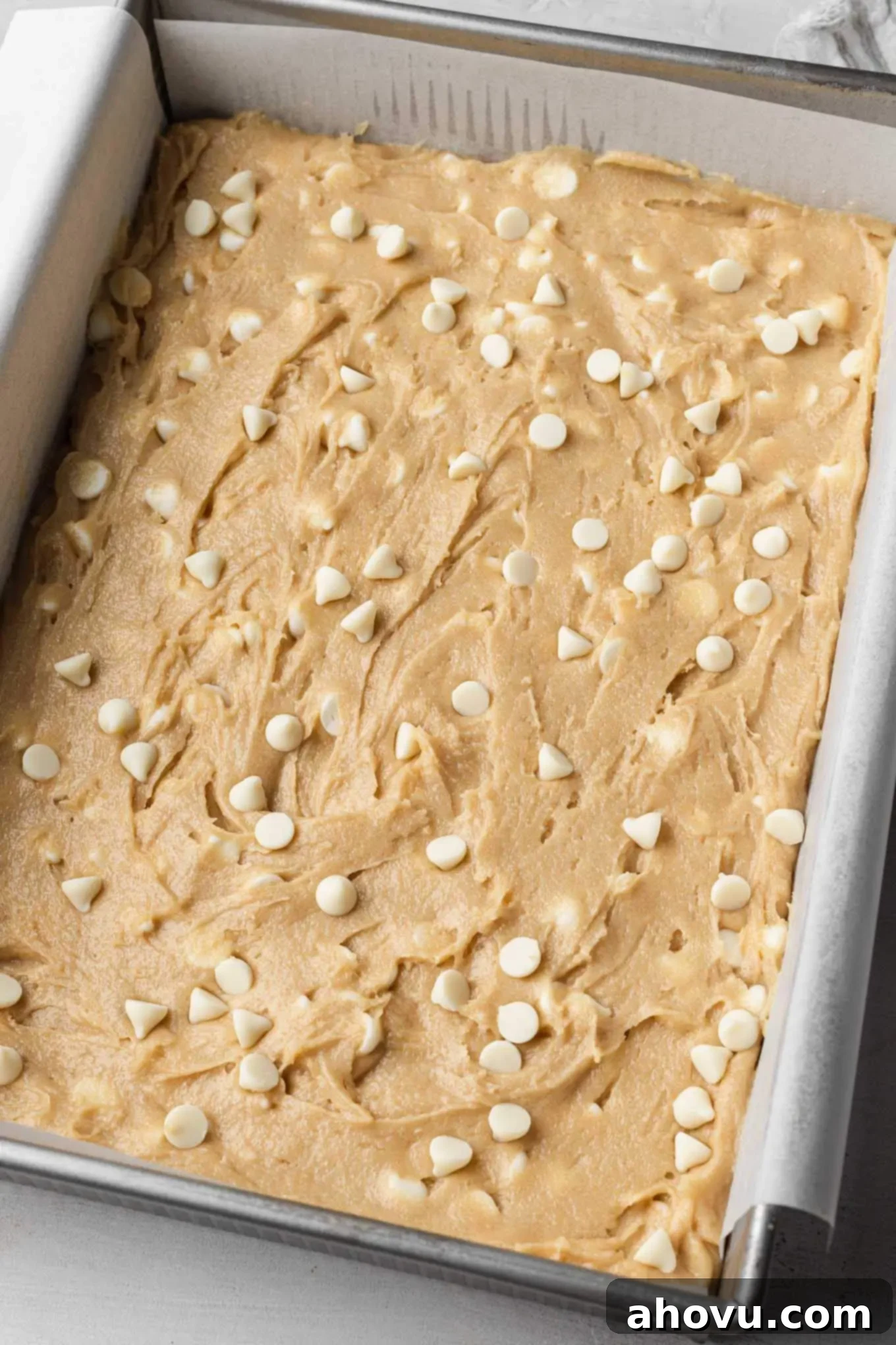 A baking pan lined with parchment paper and evenly filled with golden blondie batter, ready to go into the oven.