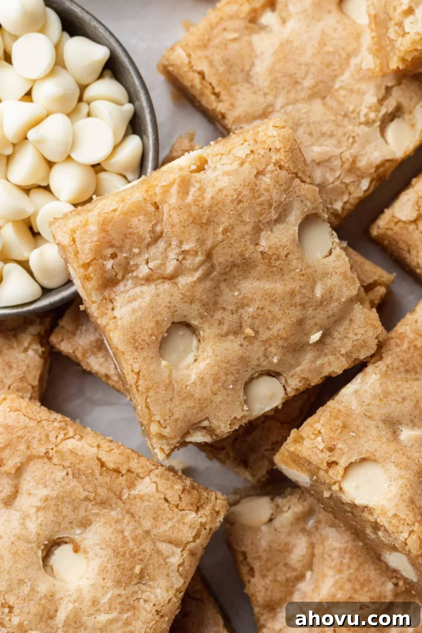 A close-up, overhead view of perfectly sliced blondies, displaying their rich vanilla color and abundance of white chocolate chips, alongside a small cup of chips.