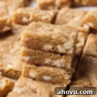 A stack of golden brown blondies with melted white chocolate chips, surrounded by more sliced bars on a wooden surface.
