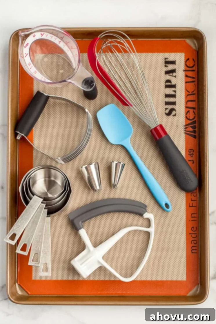 A baking sheet displaying multiple baking tools such as a whisk, measuring cups, and piping tips, showcasing essential kitchen equipment for bakers.