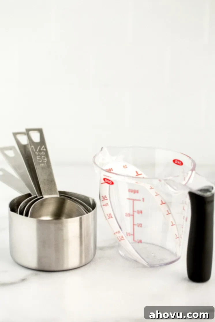 A set of metal measuring cups and a plastic angled liquid measuring cup sitting on a marble counter, highlighting precise measurement tools.