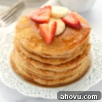 Wholesome Wheat Stacks 6 A stack of whole wheat pancakes topped with strawberry, banana slices, and maple syrup.