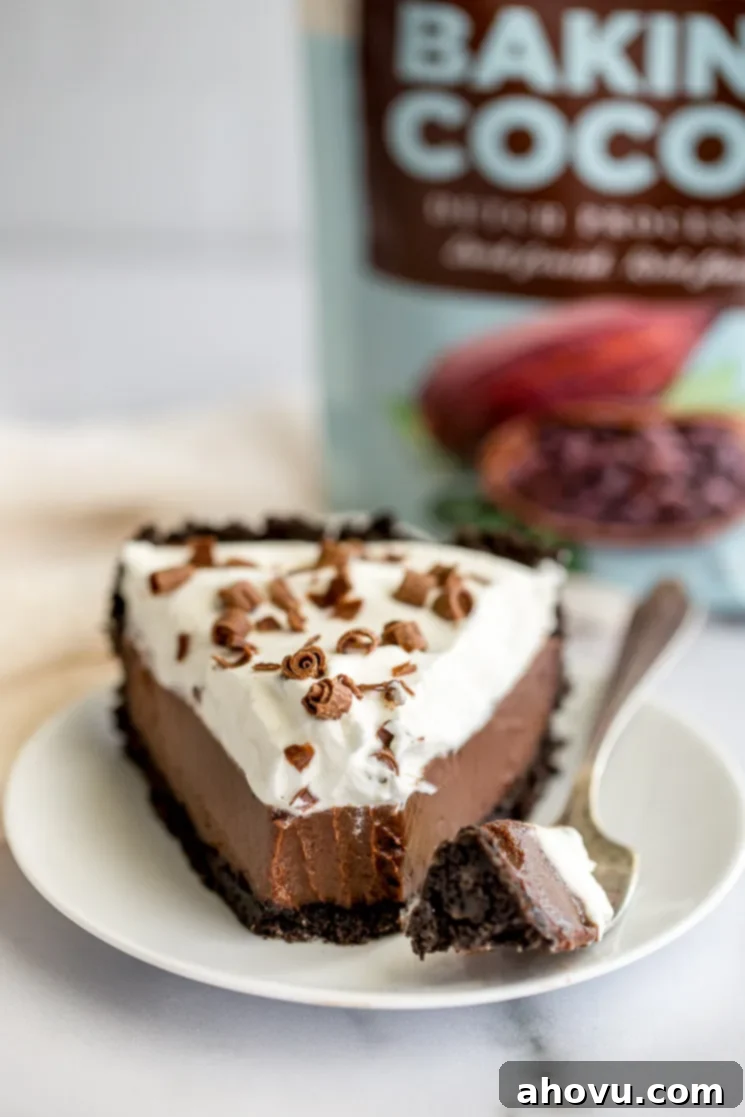 A pristine slice of homemade chocolate cream pie presented on a simple white plate, highlighting its smooth filling and generous whipped cream topping.
