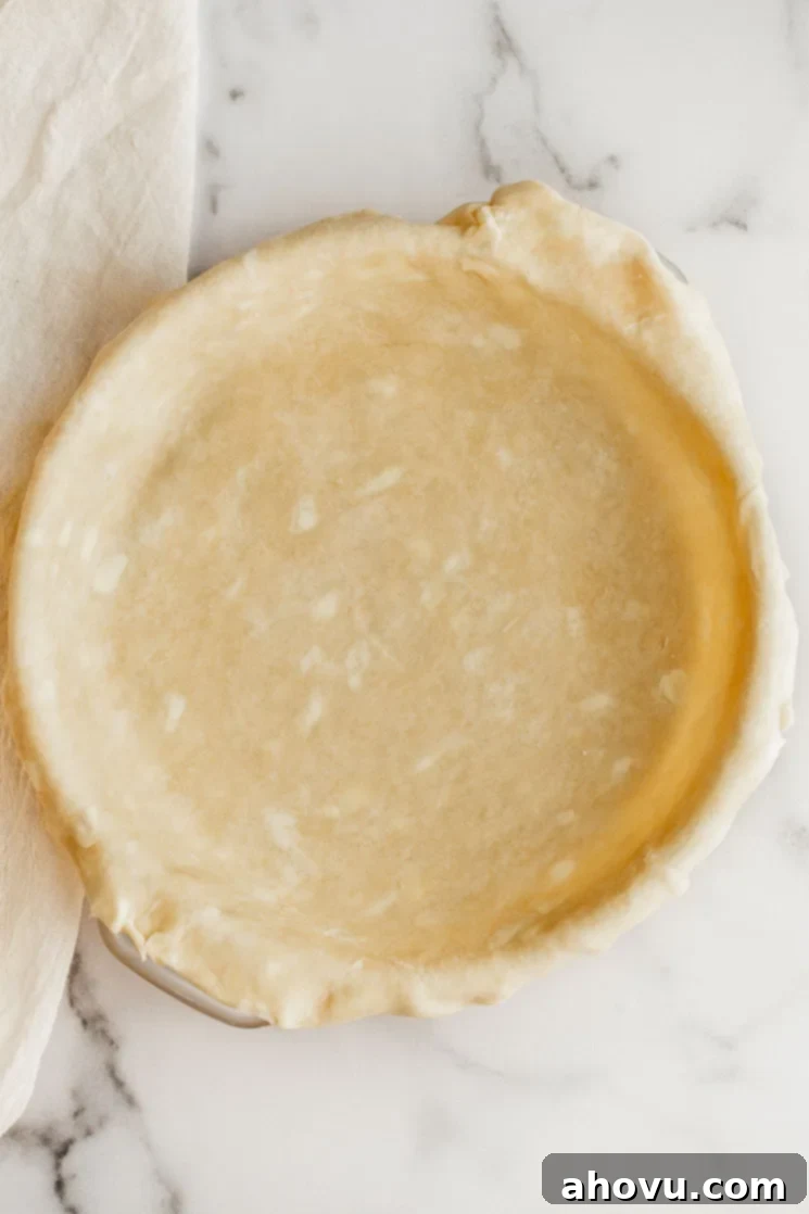 A homemade pie crust in a pie plate resting on a marble surface.