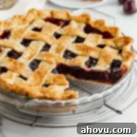 A cherry pie sitting on a wire rack with a slice taken out of it.