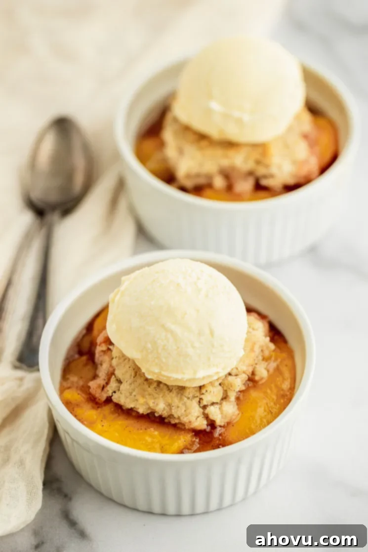 Grandma's Classic Peach Cobbler 2 A white ramekin on a marble surface filled with peach cobbler and scoop of vanilla ice cream on top, ready to be enjoyed.