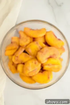 A bowl filled with freshly sliced peaches coated in cinnamon, corn starch, and sugar, ready for the cobbler filling.