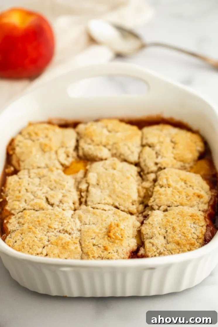 Grandma's Classic Peach Cobbler 4 A peach cobbler fresh out of the oven, golden brown and bubbling, with an antique serving spoon resting on the side and a fresh peach in the background.