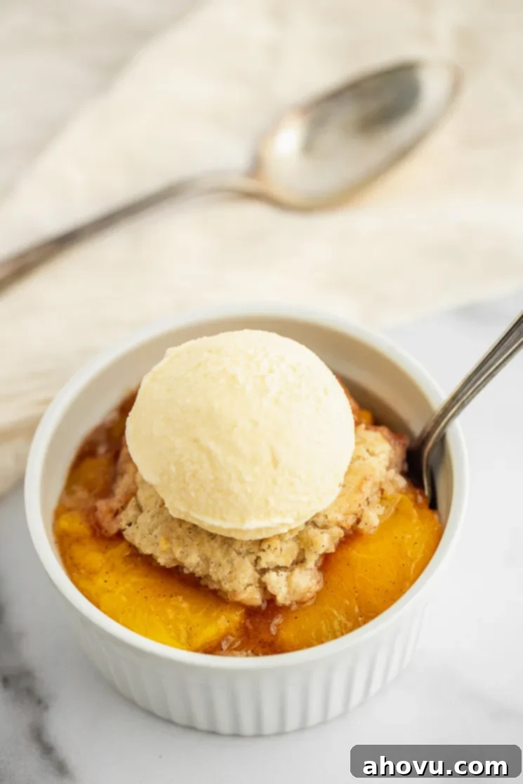 Grandma's Classic Peach Cobbler 5 A white ramekin on a marble surface filled with peach cobbler and a scoop of ice cream on top, ready for a close-up.